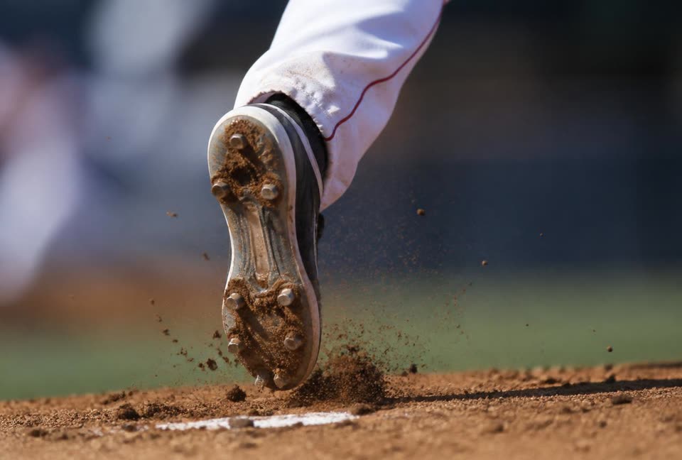 Close-up of a pitcher's back foot driving off the rubber, metal cleats digging into the dirt of the mound