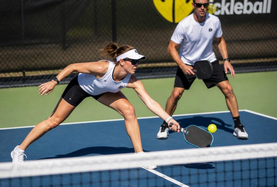 Pickleball player lunging low at the kitchen line to reach a dink, court shoes gripping the concrete